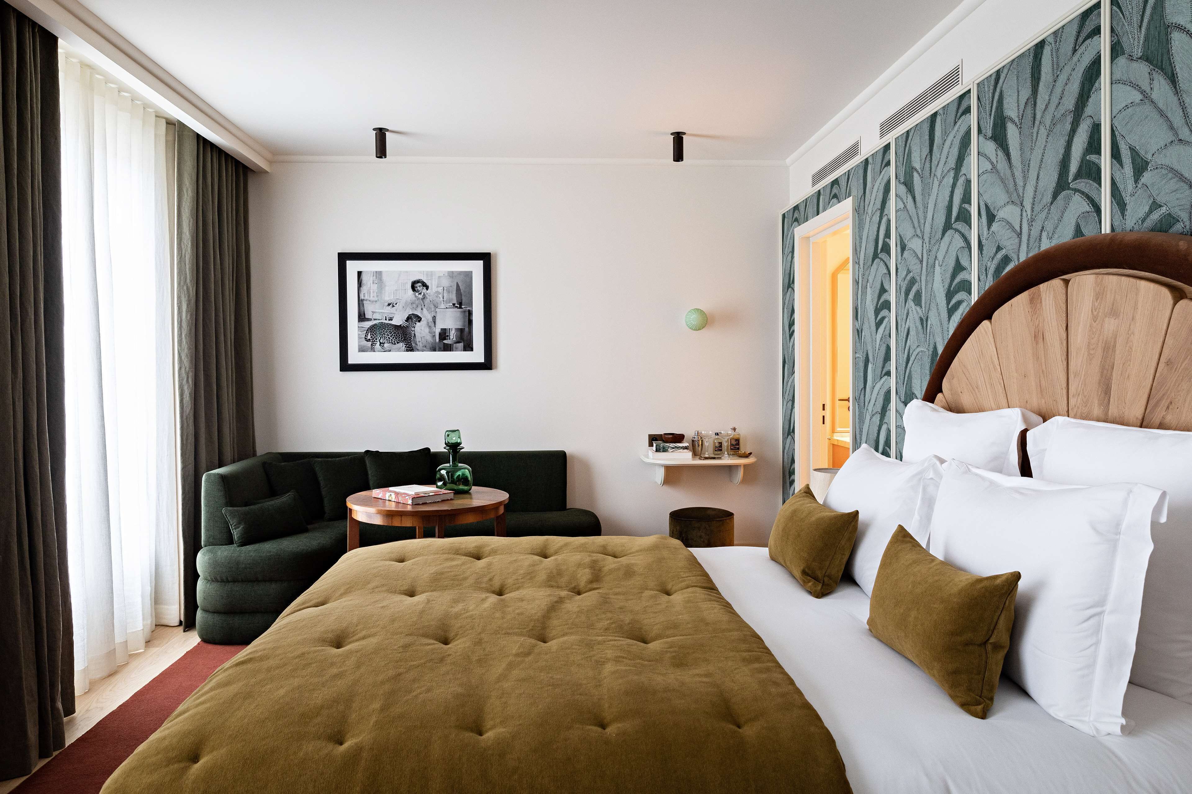 Ein Hotelzimmer mit einem großen Bett, einem grünen Sessel, einem kleinen runden Tisch und einem gerahmten Bild an der Wand.