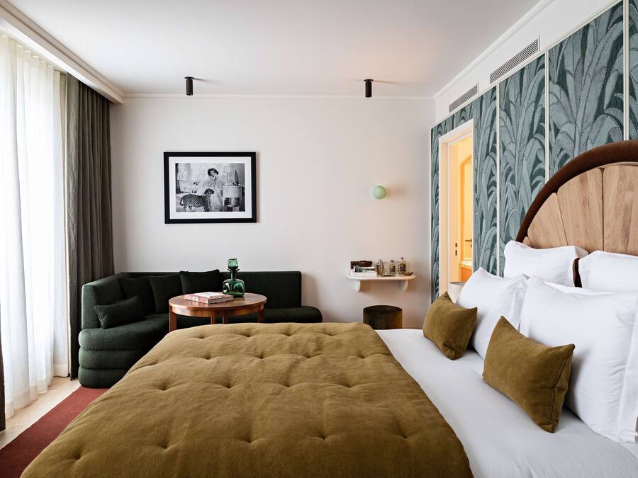 Ein Hotelzimmer mit einem großen Bett, einem grünen Sessel, einem kleinen runden Tisch und einem gerahmten Bild an der Wand.