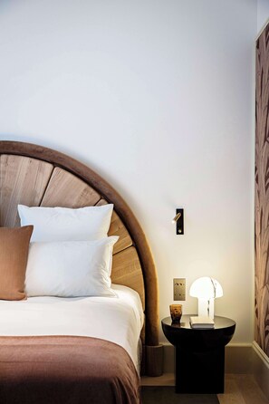 A bed with a wooden headboard, a bedside table with a lamp, and a wall-mounted light switch. - Hôtel Florida Paris (Paris)