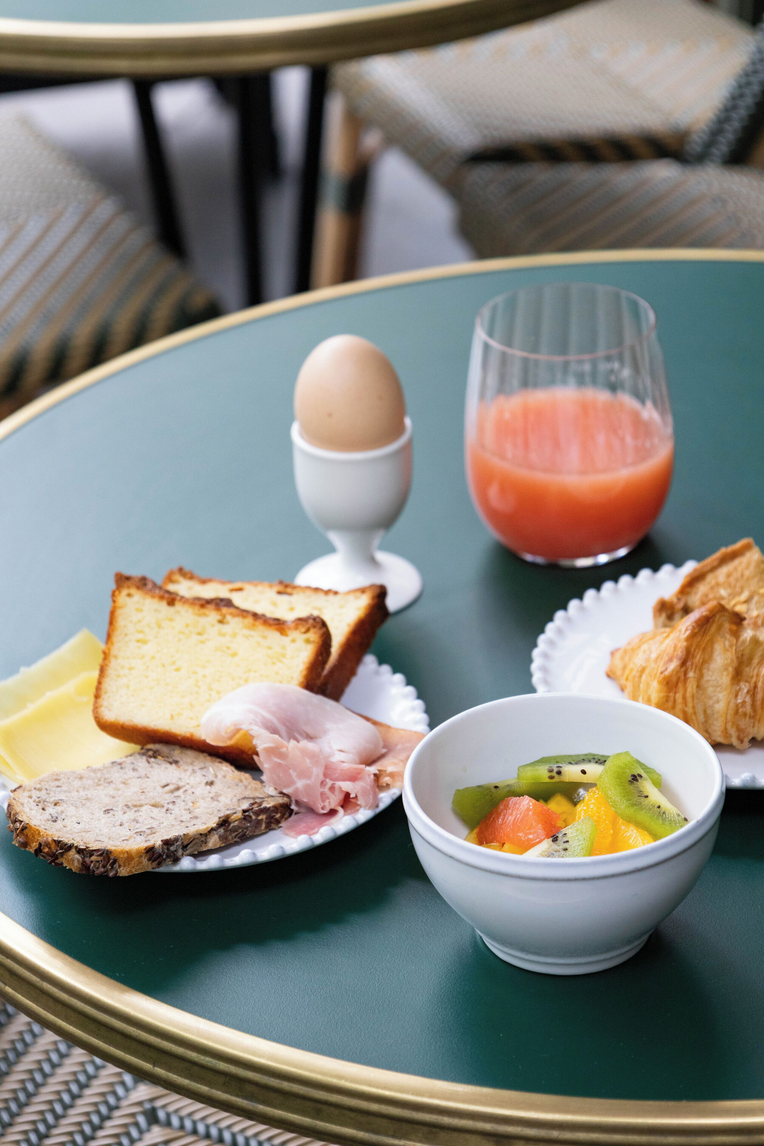 Una mesa de desayuno con tostadas, huevos, jugo, croissants y un bol de fruta.