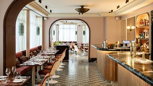 A restaurant with a long dining table, cushioned seating, a bar area, and a large mirror. - Hôtel Florida Paris (Paris)