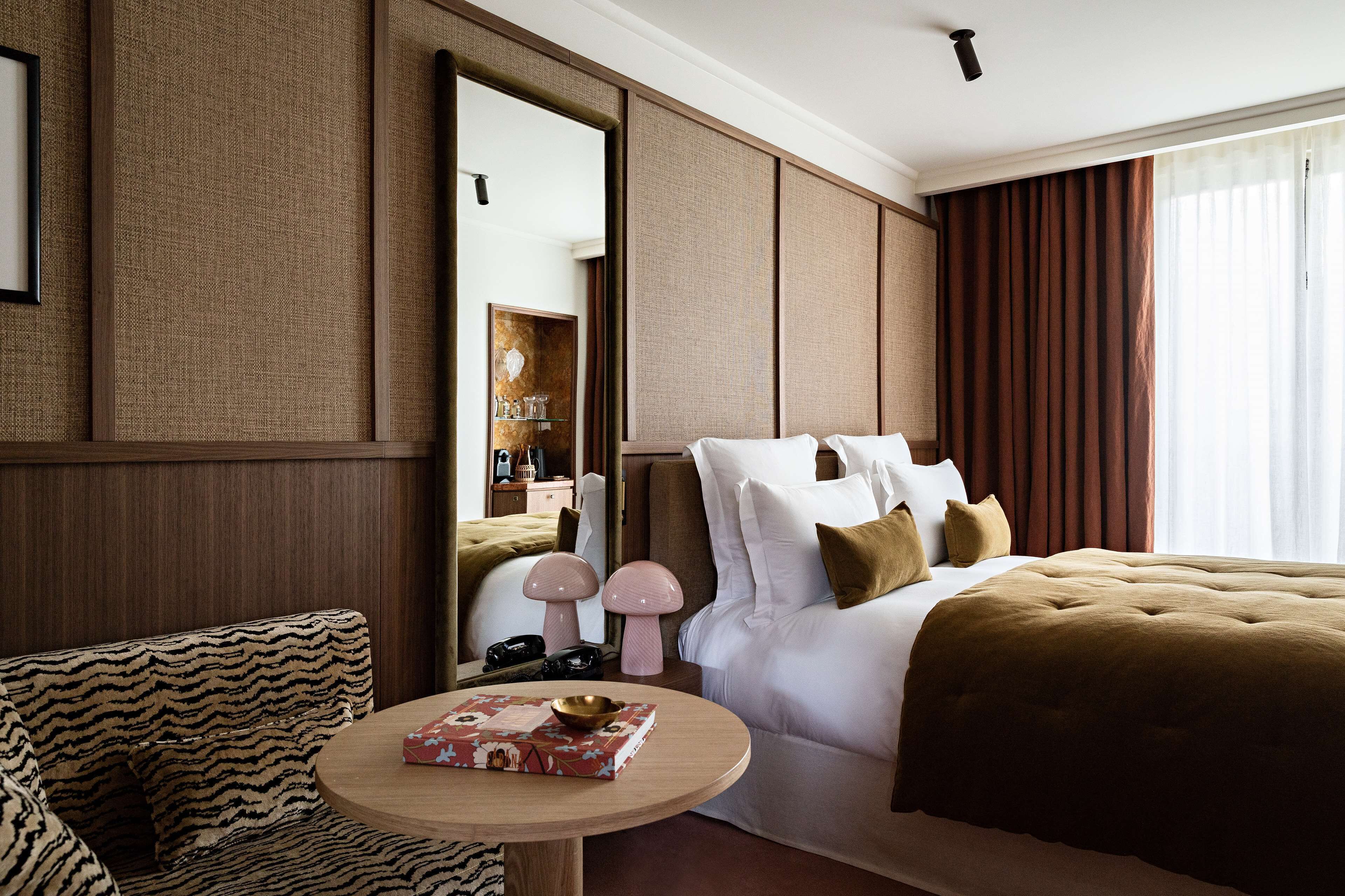 A hotel room with a large bed, a round table with a book, a sofa, and a mirror.