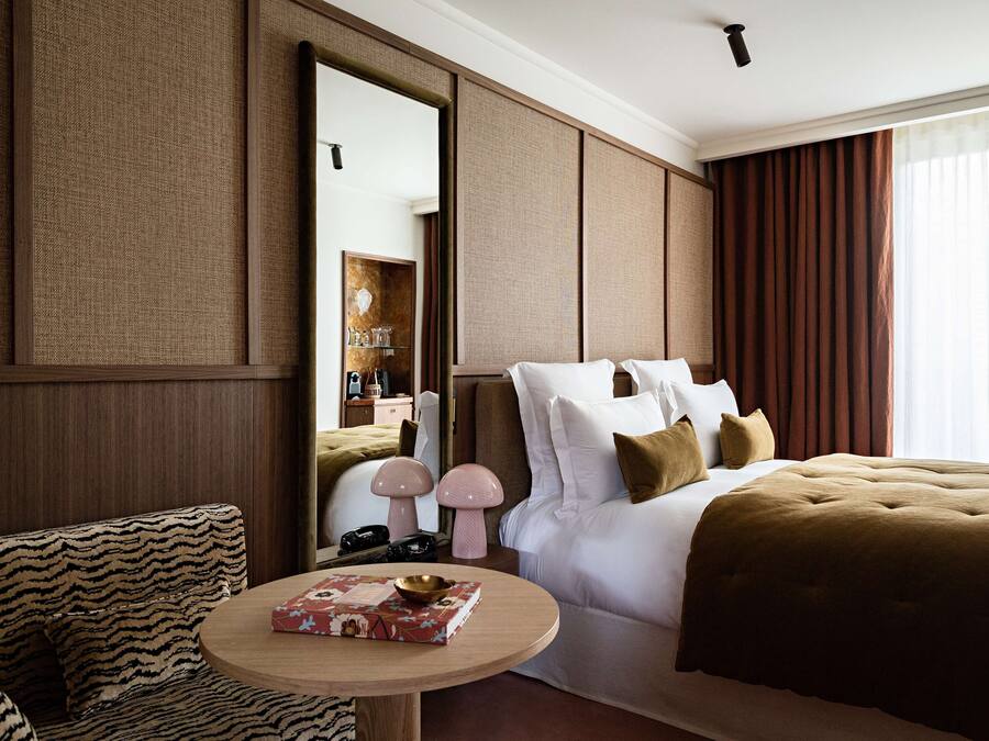 A hotel room with a large bed, a round table with a book, a sofa, and a mirror.