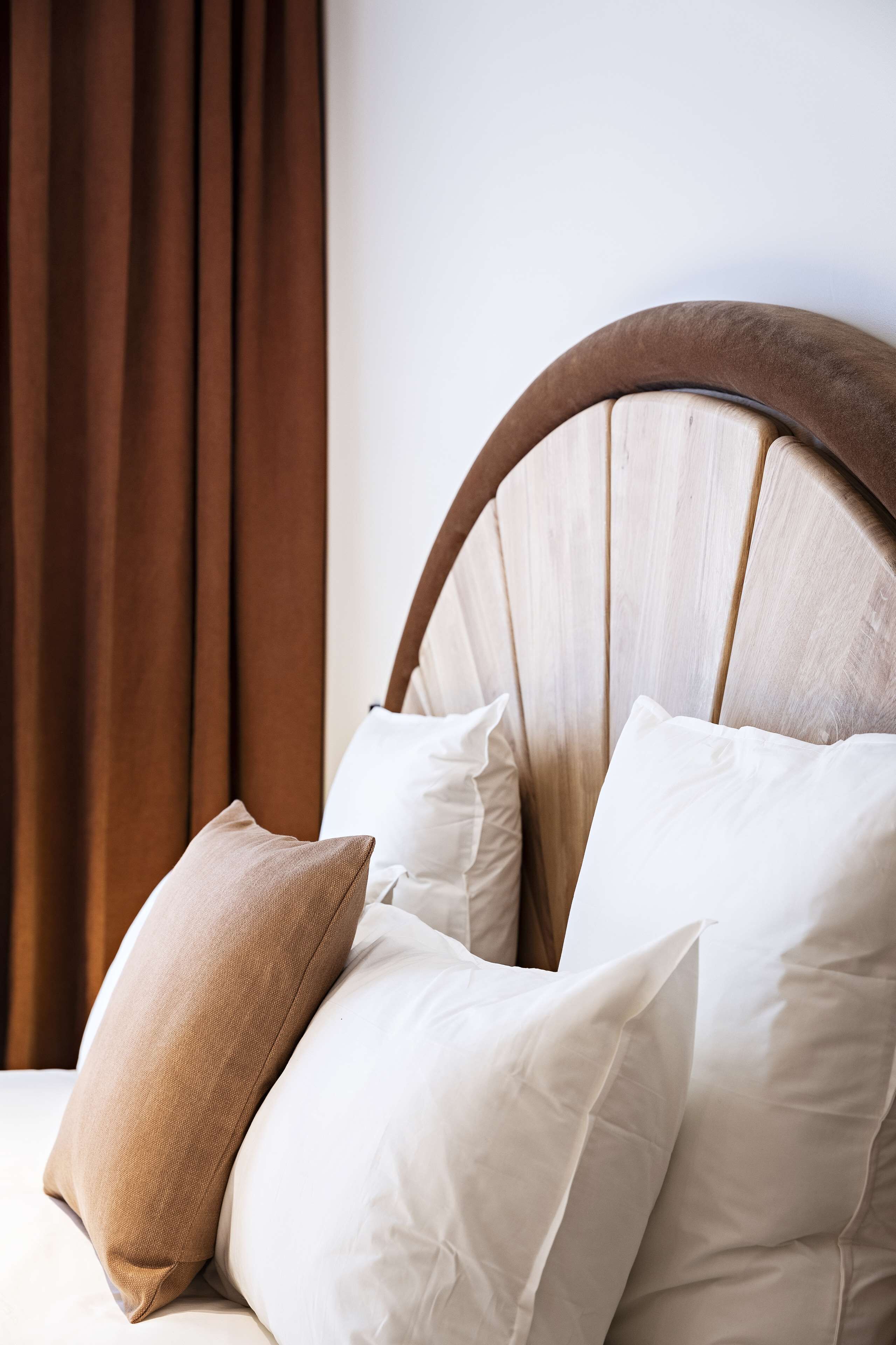 A bed with a wooden headboard, two pillows, and brown curtains.