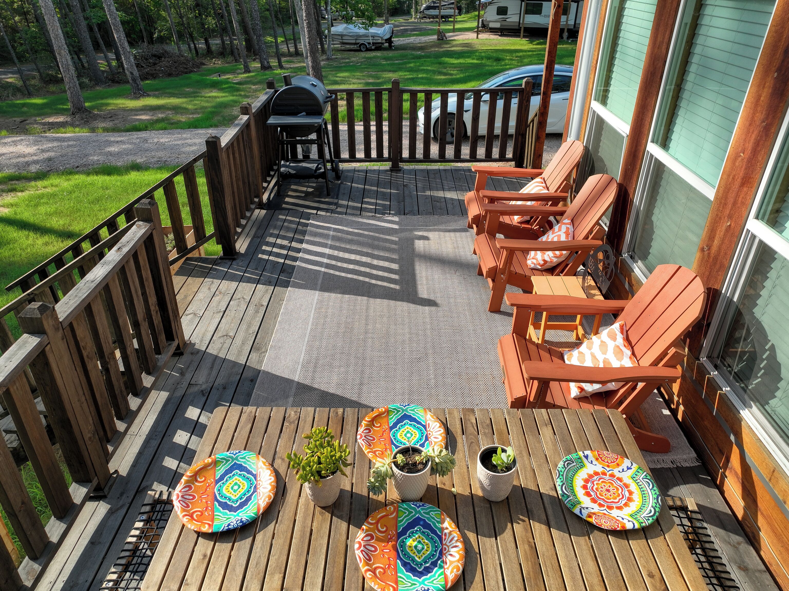 Una terraza de madera con una parrilla, muebles de exterior con cojines y plantas en macetas.