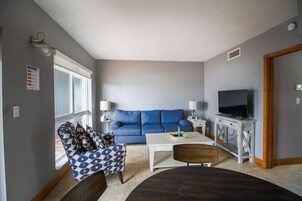 A living room with a blue sofa, a white coffee table, a TV on a wooden stand, and patterned armchairs.