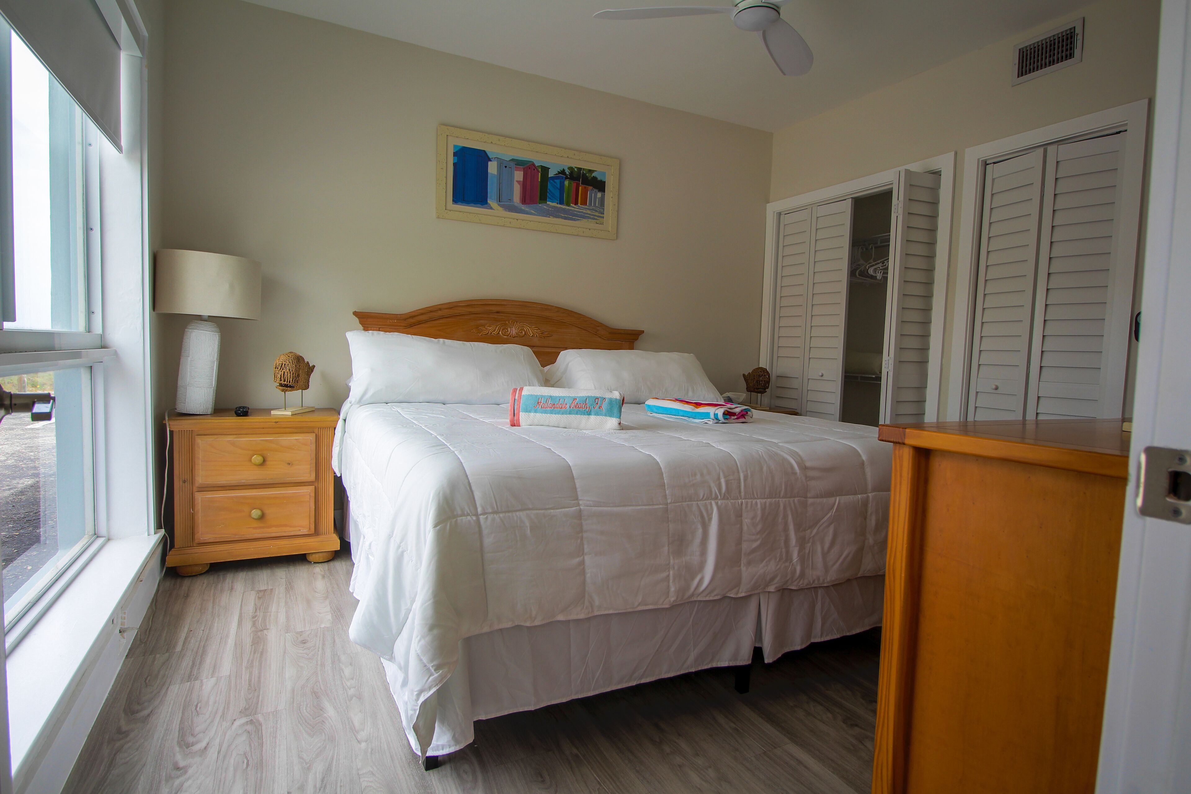 A bedroom with a bed, a nightstand, a lamp, a painting, and a closet.
