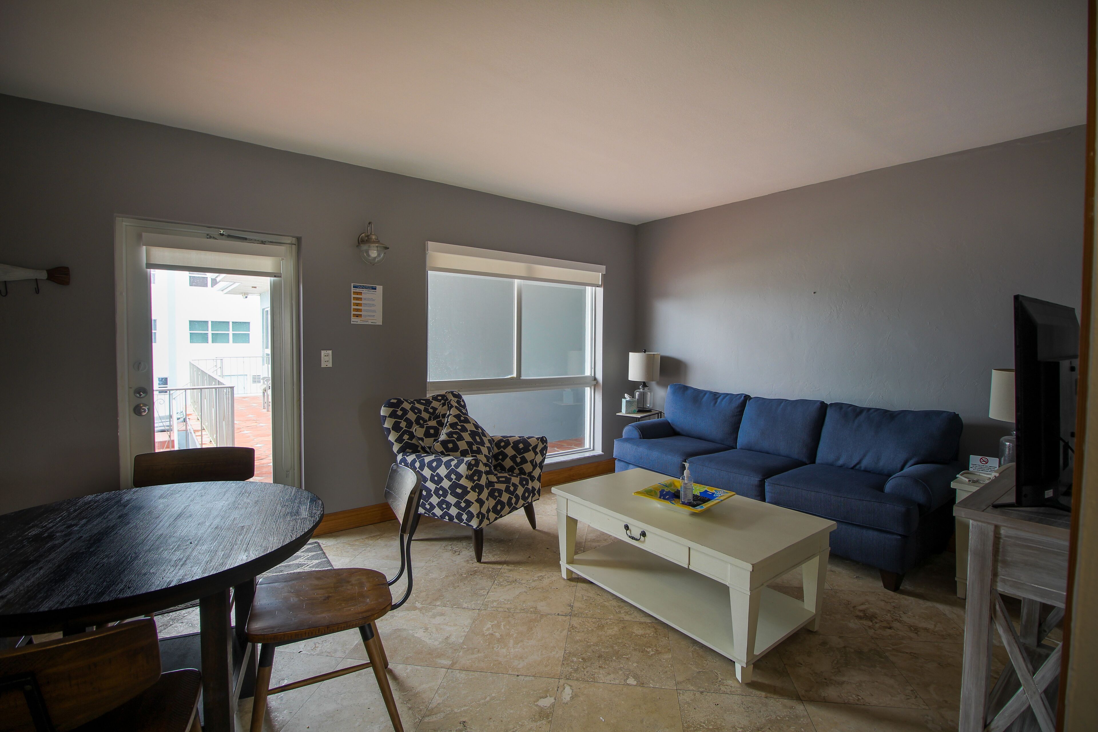 A living room with a dining table, a blue sofa, a patterned armchair, and a television.