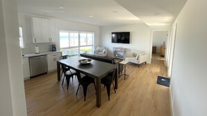 Un vaste espace de vie comprenant une table à manger en bois, des canapés blancs et une grande fenêtre donnant sur la plage.