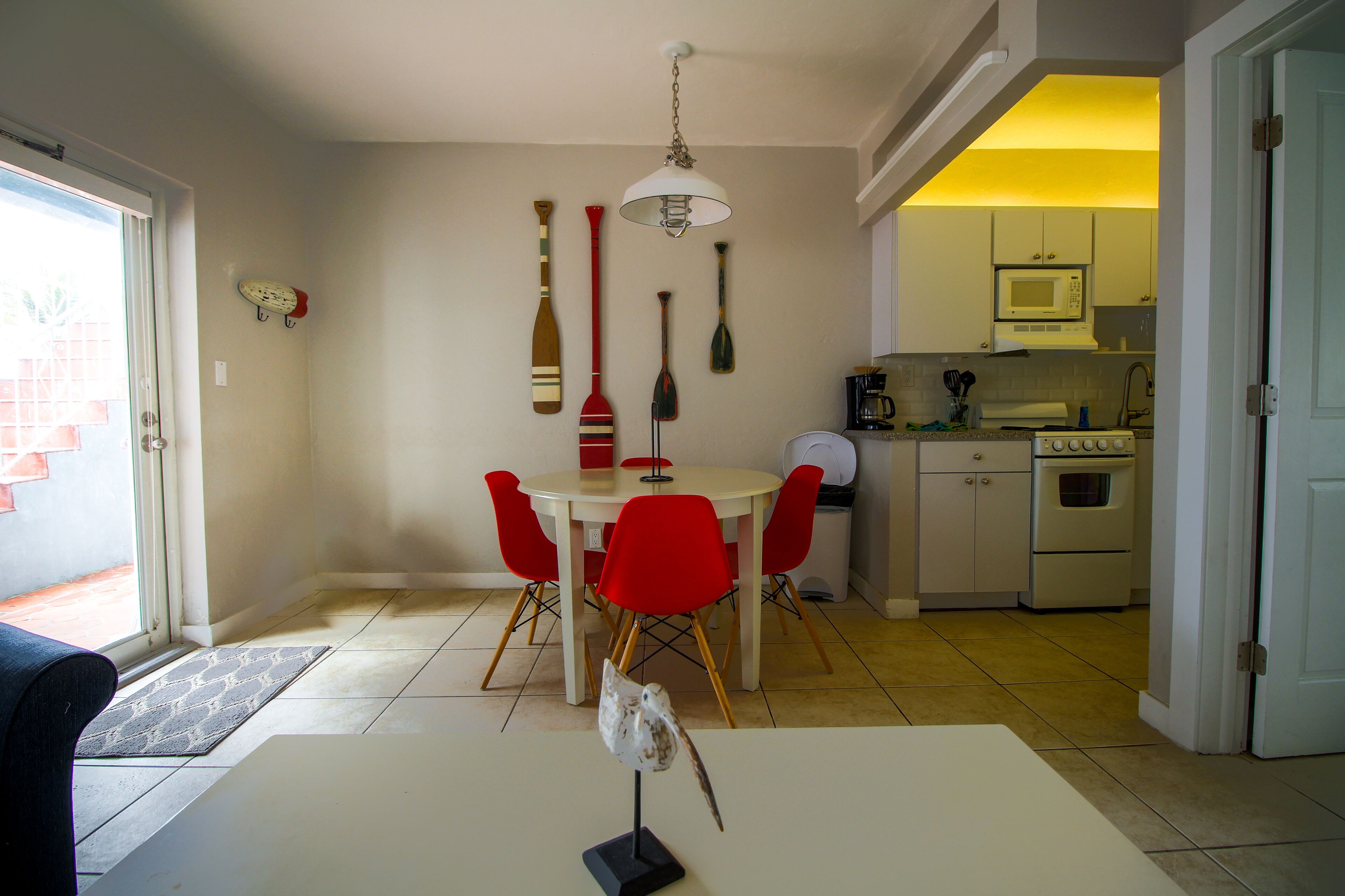 Ein Essbereich mit einem weißen Tisch und roten Stühlen, eine Küche mit Mikrowelle und Herd sowie eine Tür zu einem anderen Raum.