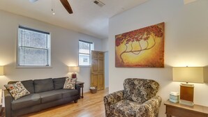Una sala de estar con un sofá de cuero oscuro, un sillón estampado, piso de madera y un cuadro grande en la pared.