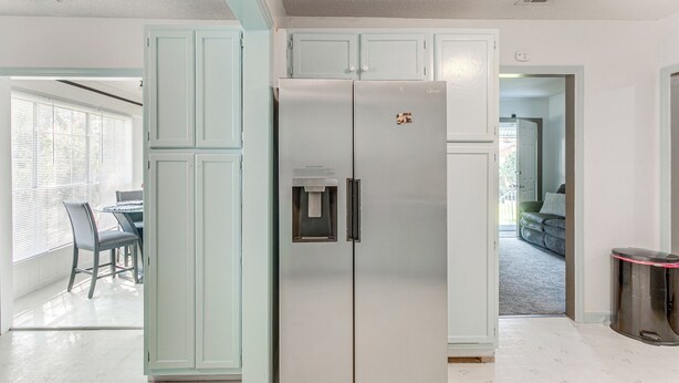 Una cocina con un refrigerador de doble puerta, una mesa de comedor con sillas y una ventana con persianas.