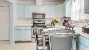 Una cocina con armarios azul claro, microondas, estufa y una mesa de comedor con sillas.