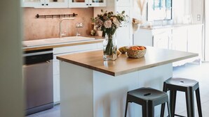 Une cuisine moderne dotée d’un îlot central, de poutres apparentes en bois au plafond et d’un luminaire suspendu.