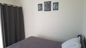 Un dormitorio con una cama, una cortina oscura y tres cuadros enmarcados en la pared.