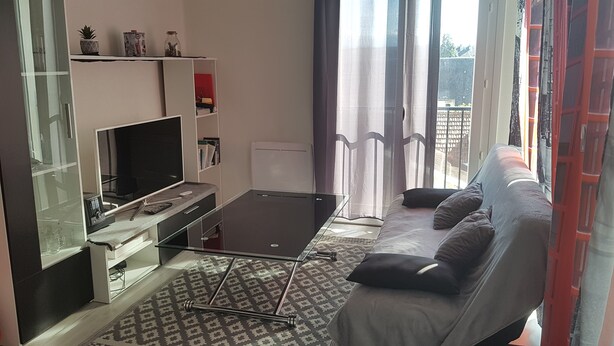 Una sala moderna con televisor de pantalla plana, una mesa de centro de vidrio, un sofá con cojines y una estantería.