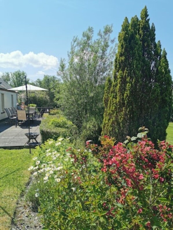 Un espace patio aménagé avec du mobilier d’extérieur, un grand arbre à feuilles persistantes et des plantes à fleurs.