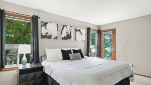 Une chambre à coucher avec un grand lit, une table de chevet, une fenêtre avec des rideaux et des œuvres d’art abstraites accrochées au mur.