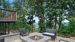 Une terrasse extérieure dotée d’un foyer, de sièges et d’une plateforme offrant une vue sur une zone boisée.