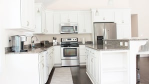 A modern kitchen with white cabinets, stainless steel appliances, granite countertops, and a built-in oven. - Hale Aloha: An Aloha-Inspired Escape in the OBX (Kill Devil Hills)