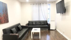 A living room with two black sofas, a white coffee table, and a flat-screen TV mounted on the wall. - Spacious 3 beds Loft with Parking($14/day) (Montréal)