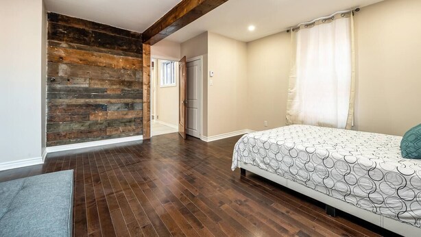 A bedroom with a wooden accent wall, a bed with a patterned bedspread, and a wooden floor. - Spacious 3 beds Loft with Parking($14/day) (Montréal)