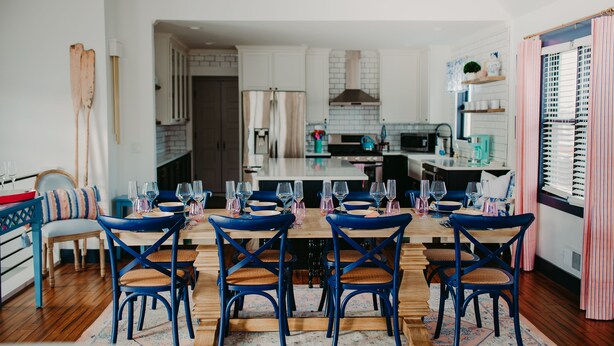 A dining area with a wooden table and blue chairs, a kitchen in the background, and a striped curtain on the right. - NEW boutique, luxury rental in Downtown Petoskey! Dogs welcome! (Petoskey)