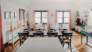 A dining area with a white table set for four, surrounded by chairs, with a sofa and a TV in the background. - NEW boutique, luxury rental in Downtown Petoskey! Dogs welcome! (Petoskey)