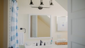 A bathroom with a white sink, three lights, a large mirror, and a towel rack. - NEW boutique, luxury rental in Downtown Petoskey! Dogs welcome! (Petoskey)