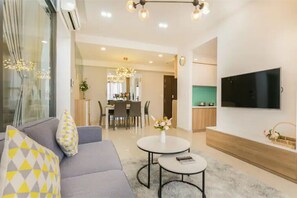 A modern living room with a sofa, two round tables, a flat-screen TV, and a dining area in the background.