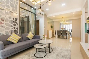 A modern living room with a grey sofa, two round coffee tables, and a dining area with a chandelier.