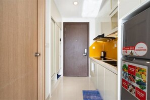 A narrow hallway with a wooden door, a kitchen area with a yellow wall, and a refrigerator with a food advertisement.