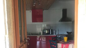 A kitchen with a red cabinet, a microwave, and a sink. There is a dining table with chairs and a yellow vase. - country house (Frayssinet-le-Gélat)