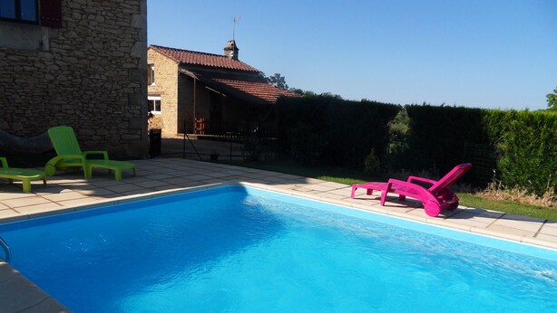 A swimming pool with two lounge chairs, one green and one pink, and a stone building in the background. - country house (Frayssinet-le-Gélat)