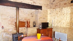 A rustic stone-walled room with a round wooden table covered by a patterned tablecloth, a wooden cabinet, a television, and a fireplace. - country house (Frayssinet-le-Gélat)