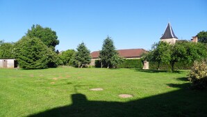 A grassy courtyard with a stone wall, trees, and a building with a tiled roof. - country house (Frayssinet-le-Gélat)