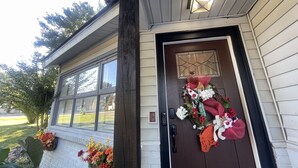 Una casa con puerta principal de color marrón oscuro, una ventana adornada con una corona y un pequeño porche con flores.