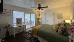 Un dormitorio con cama, escritorio, silla, ventilador de techo y puerta corrediza de vidrio al exterior.