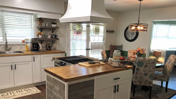 Una cocina con armarios blancos, una isla central y una zona de comedor con sillas estampadas.