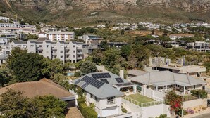 A residential area with modern houses, some with solar panels, surrounded by mountains and greenery. - Camps Bay Echo Garden Apartment (Cape Town)
