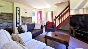 A living room with a sofa, a coffee table, a TV, and a staircase. - Honeysuckle Cottage (Llanfyrnach)