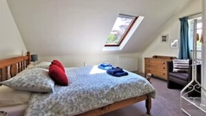 A bedroom with a sloped ceiling, a skylight, a bed with patterned bedding, a dresser, and a chair. - Honeysuckle Cottage (Llanfyrnach)