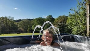 A person in a hot tub with water jets, surrounded by greenery and a clear sky. - Honeysuckle Cottage (Llanfyrnach)