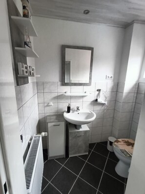 Bathroom features a pedestal sink, toilet, and storage cabinet.