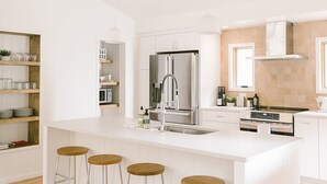 A modern kitchen with a central island, bar stools, and a stainless steel refrigerator. - Scandi Cabin on 105 acres: Hot Tub/Sauna/Views/EV, (Lansing)