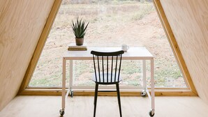 A triangular room with a table and chair, a potted plant, and a view of a natural landscape through a large window. - Scandi Cabin on 105 acres: Hot Tub/Sauna/Views/EV, (Lansing)