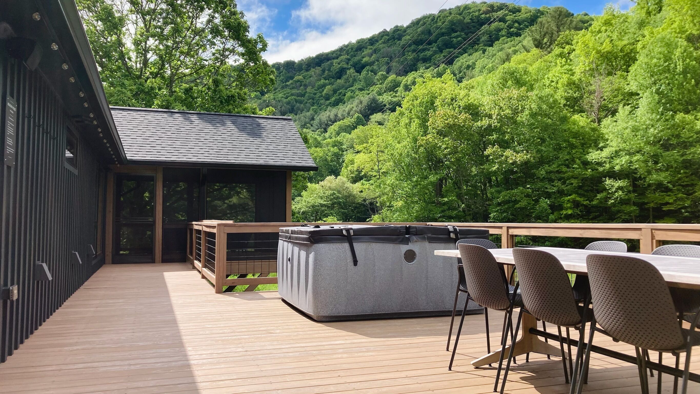 A wooden deck with a table and chairs, a hot tub, and a building with large windows.