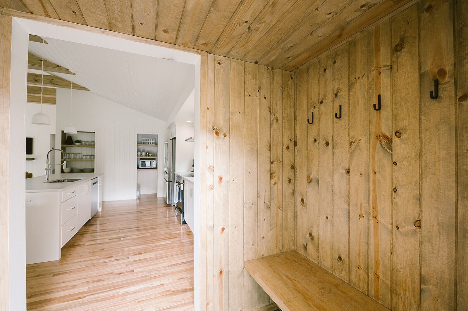 Une cuisine moderne avec des meubles blancs, un plancher en bois et un banc en bois.
