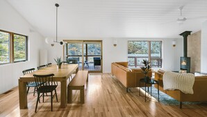 A spacious living area with a wooden dining table, chairs, a sofa, and a fireplace. - Scandi Cabin on 105 acres: Hot Tub/Sauna/Views/EV, (Lansing)