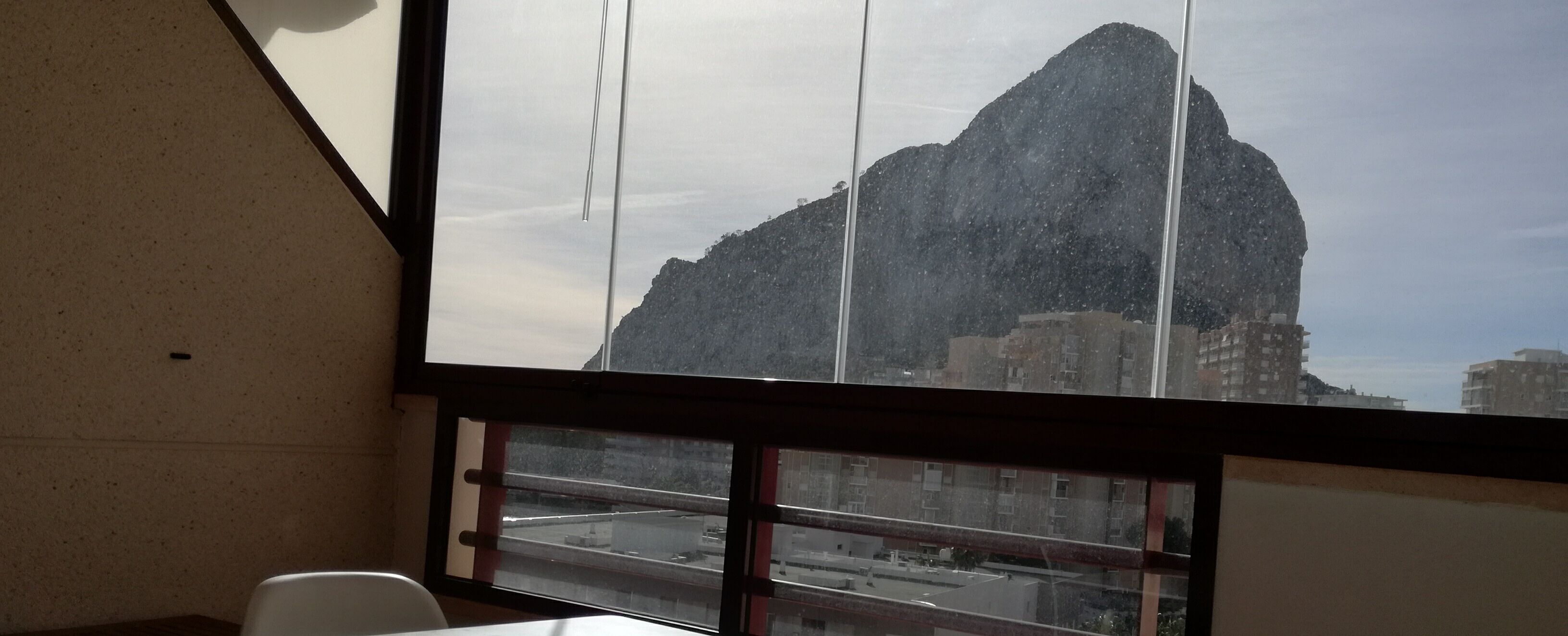 Une fenêtre donnant sur une montagne et des bâtiments.
